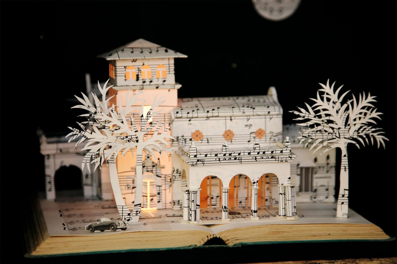 Sheet music from Prokofiev’s Romeo and Juliet is used to craft Caribbean villa model homes in paper form.